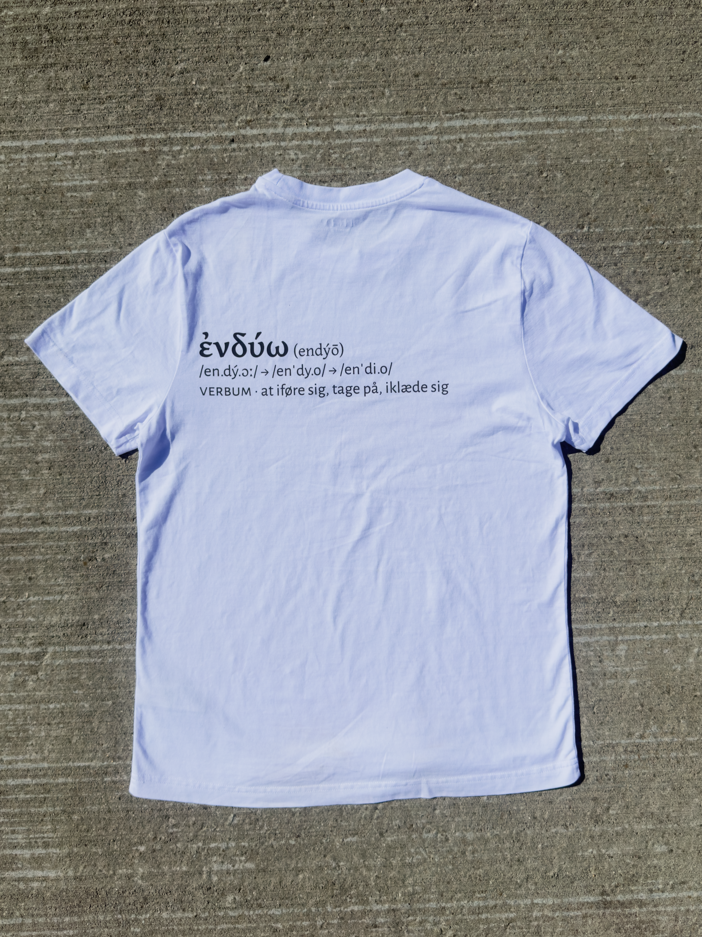Endýō – hvid kristen T-shirt liggende med ἐνδύω-ordbogsopslag på ryggen