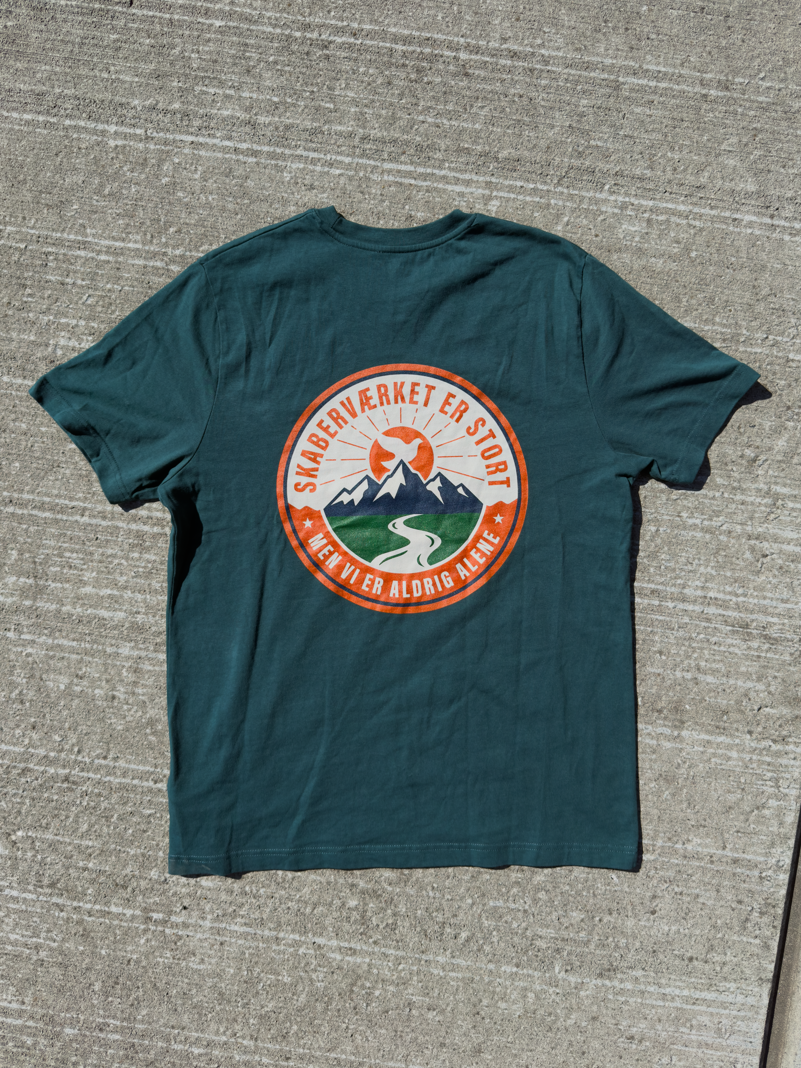 Skaberværket er stort – mørkegrøn kristen T-shirt liggende med badge-print på ryggen